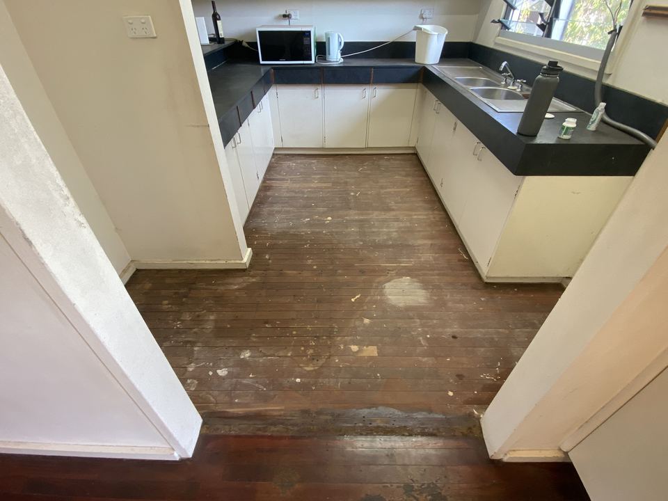 U-shaped kitchen floor before sanding, with worn, stained and scratched boards.