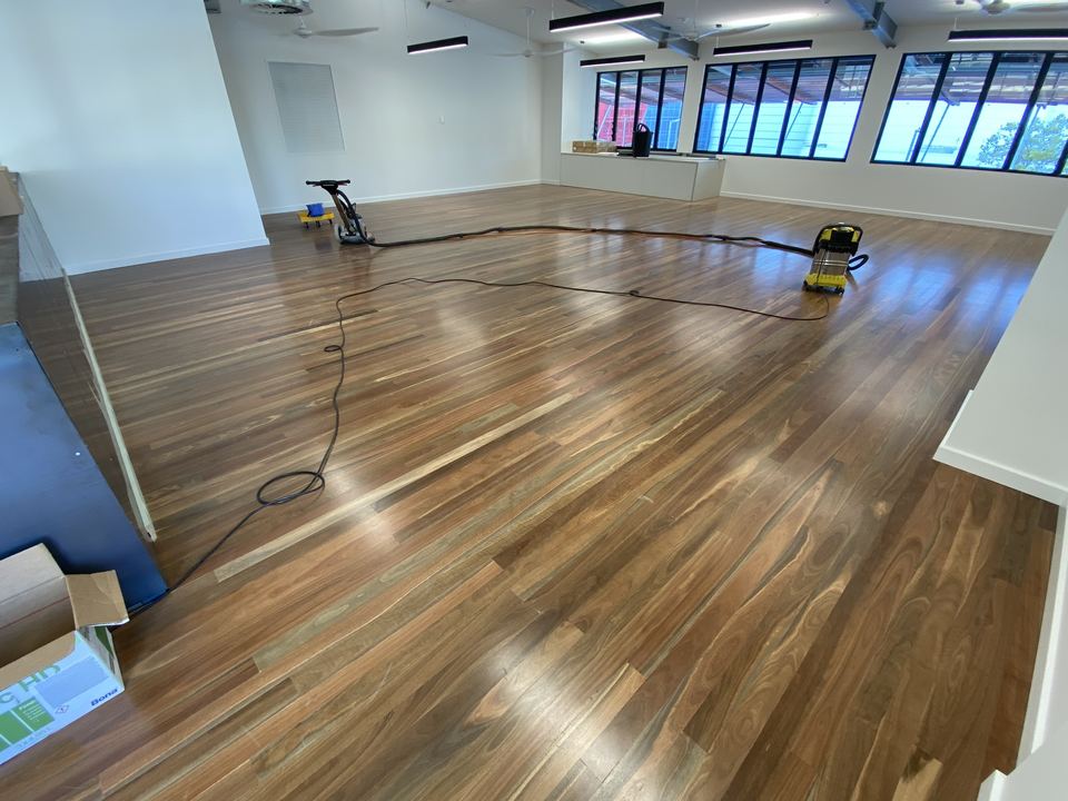 Sanding equipment in a large room with a freshly polished hardwood floor and long windows.