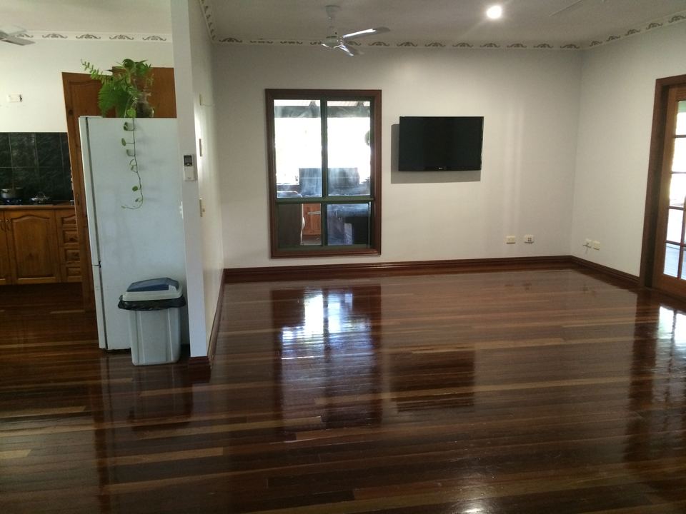 Large open room with a polished red-brown hardwood floor reflecting the windows.