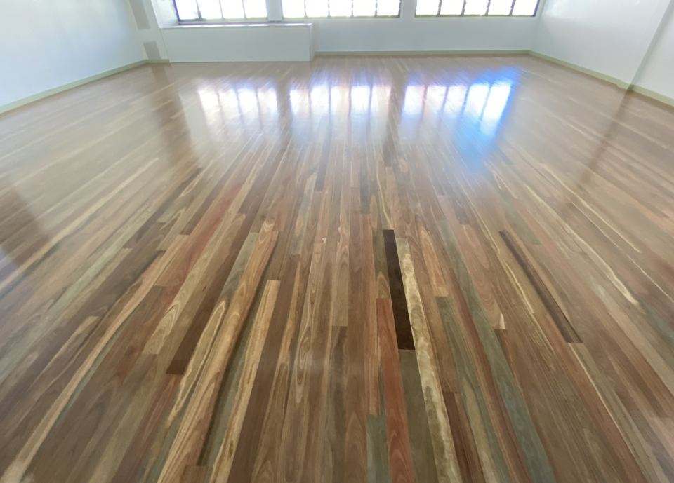 Hardwood floor part way through sanding, with freshly sanded and older boards side by side.