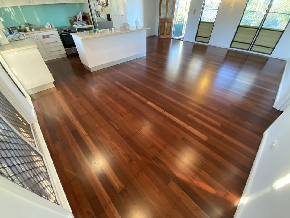 Open-plan living area with a glossy red-brown hardwood floor and a white kitchen island.