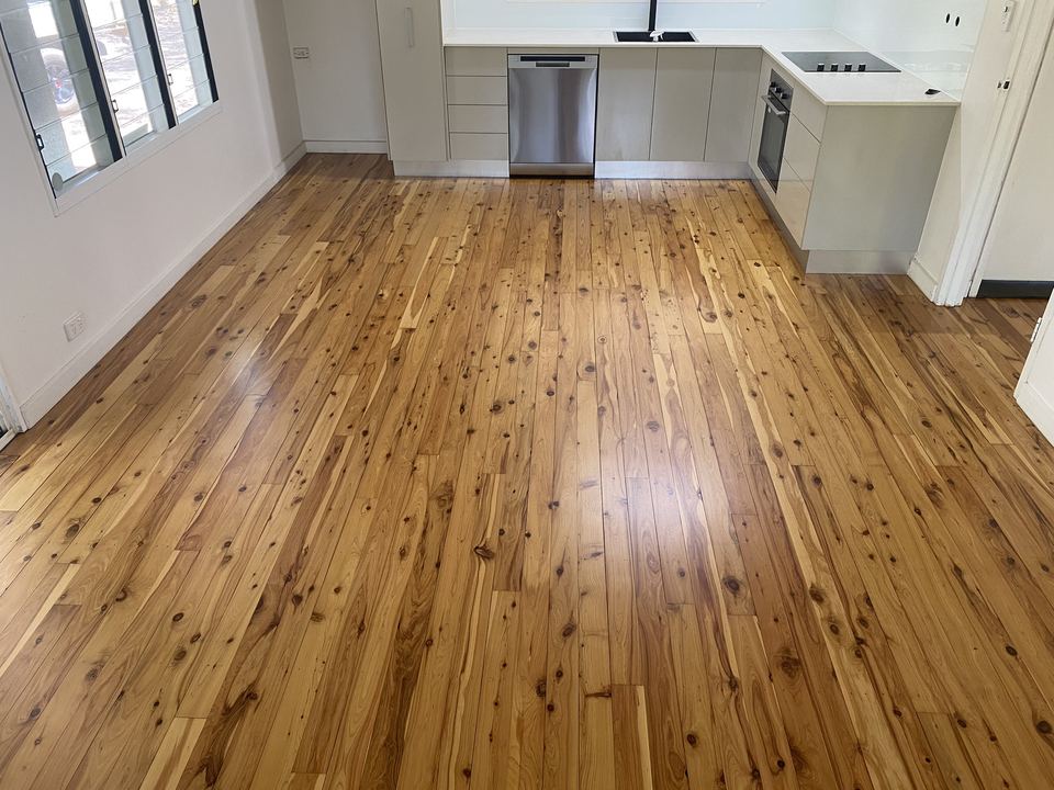Polished pine floor in an open kitchen with white cabinetry.