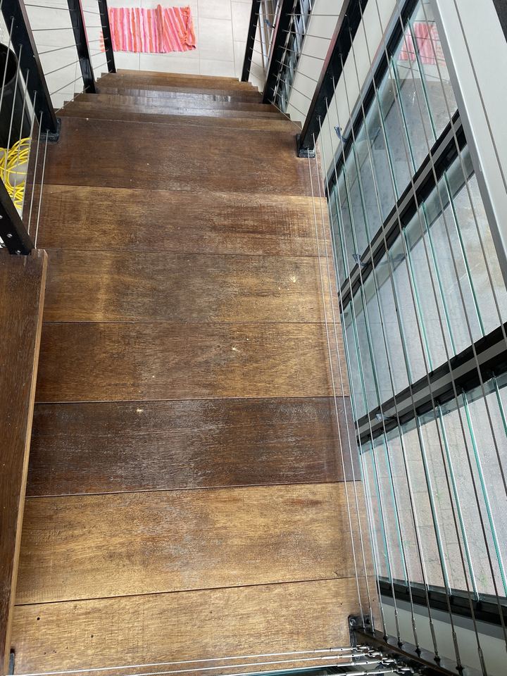 Worn timber stair landing before sanding, beside a cable balustrade.